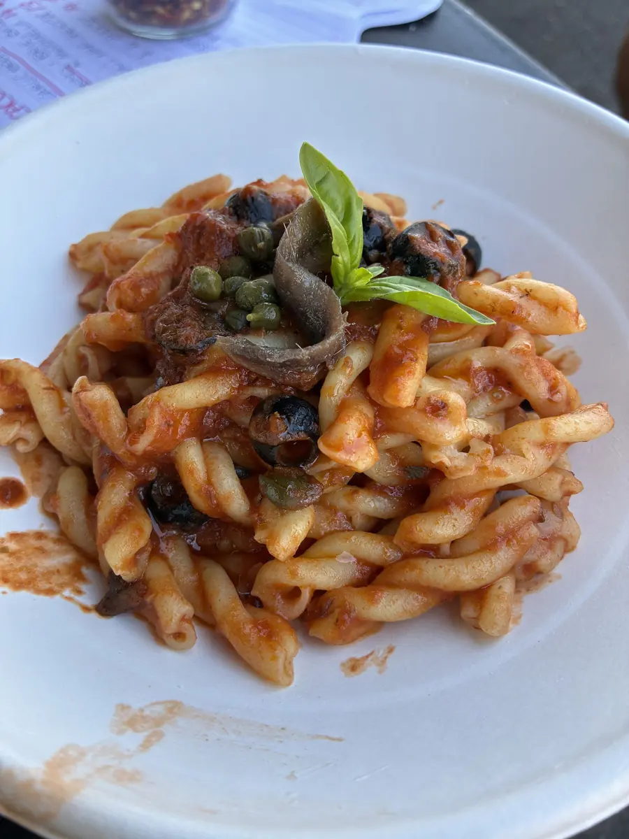 Pasta puttanesca with olives, capers and anchovy on a white plate